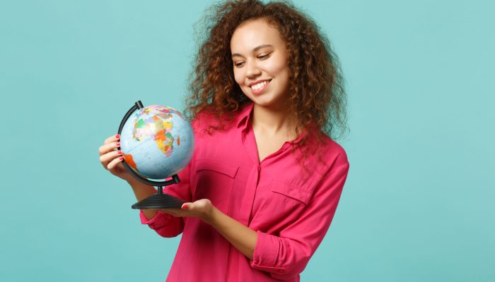 Portrait of smiling african girl in casual clothes holding in hands Earth world globe isolated on blue turquoise background in studio. People sincere emotions, lifestyle concept. Mock up copy space