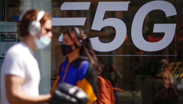 People, wearing protective face masks, walk past a 5G data network sign at a mobile phone store in Paris, France, April 22, 2021. REUTERS/Gonzalo Fuentes