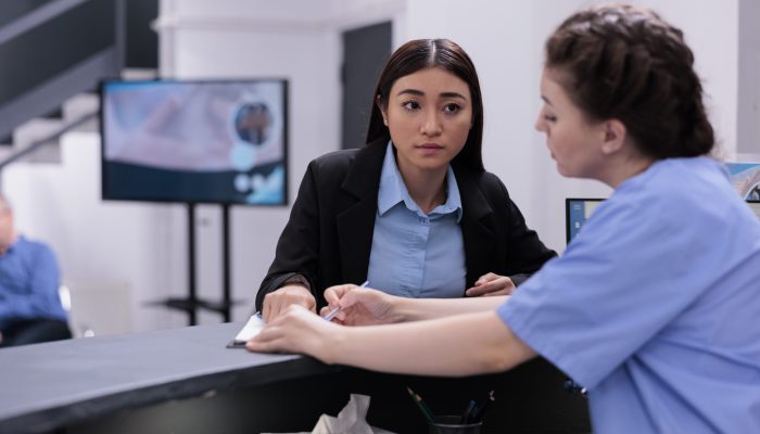 Nurse showing medical report to receptionist discussing expertise during checkup visit examination in hospital waiting room. Worker helping assistant with consultations and follow-up appointments.