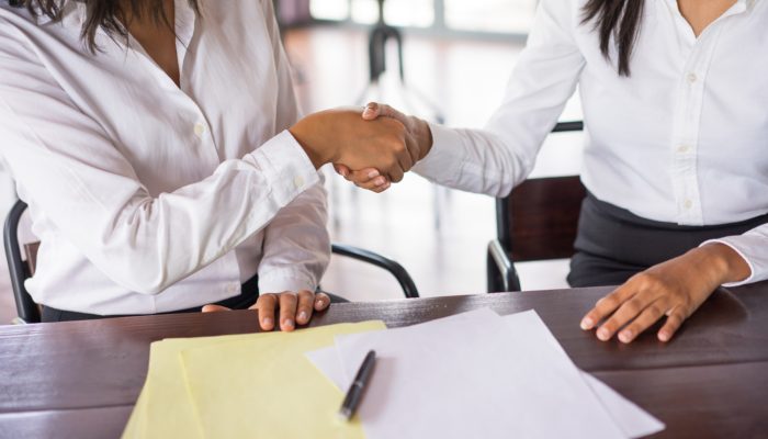 closeup-two-business-women-shaking-hands-sitting-desk