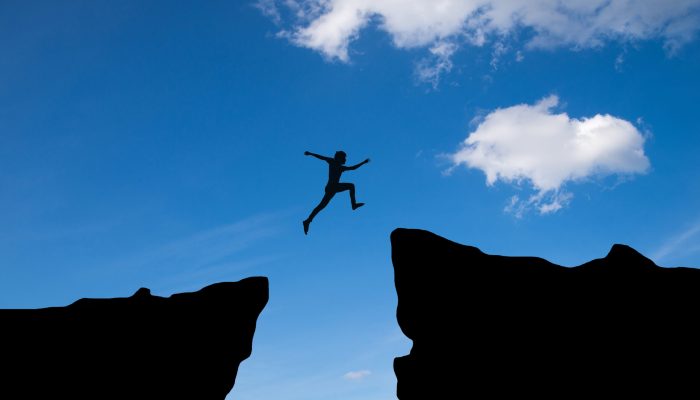 Man jump through the gap between hill.man jumping over cliff on sunset background,Business concept idea