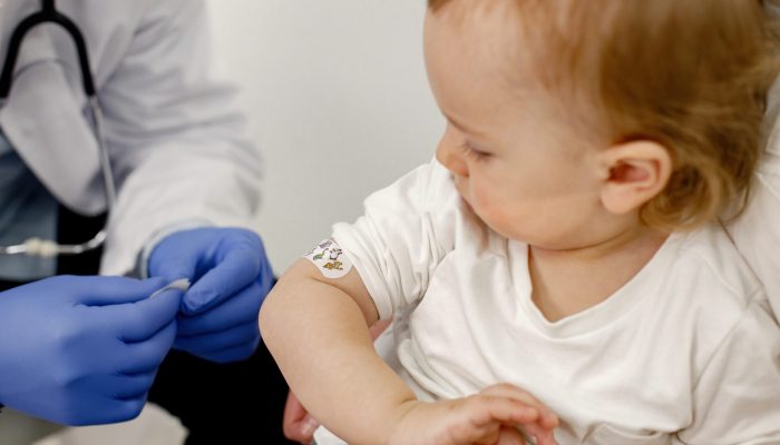 Cropped photo of a little boy in hospital. Medical worker wearing blue gloves and face mask. Boy wearing white t-shirt.