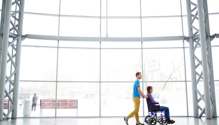 Young man pushing his girlfriend in wheelchair outdoors after shopping at mall