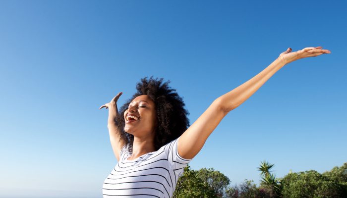 Portrait of young african woman standing outdoors with arms raised and laughing