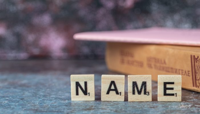 Name writing with black letters on wooden dices with an old book around. High quality photo
