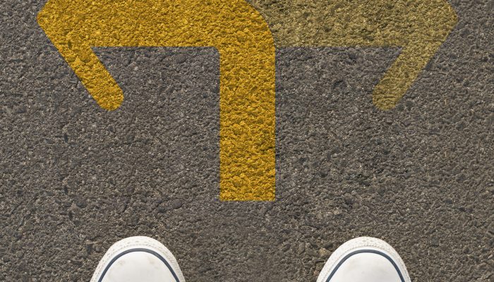 Pair of shoes standing on a road with two way yellow arrow