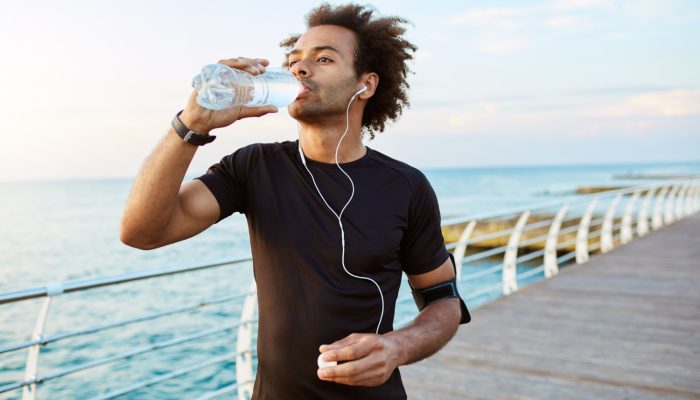stylish-afro-american-male-runner-drinking-water-out-plastic-bottle-after-cardio-workout-wearing-white-earphones-sportsman-black-sportswear-hydrating-during-outdoor-training