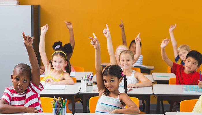 Smiling school kids raising hand in classroom at school