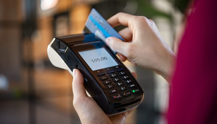 Close up of woman hands making a credit card payment with card reader machine. Credit card swipe through terminal for sale in store. Cashier hand swiping debit card after a purchase.