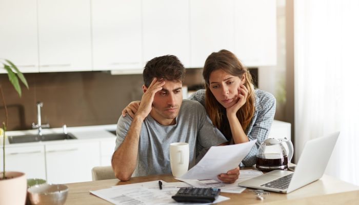 Unhappy American couple managing home accounts in kitchen, trying to save some money by cutting family expenses. Finances, bankruptcy, taxes, money, accounting and financial problems concept