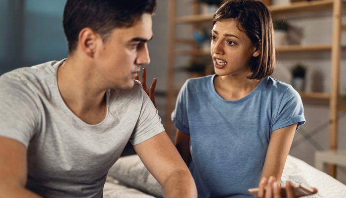 Young couple having a conflict and arguing in the bedroom. Focus is on woman.