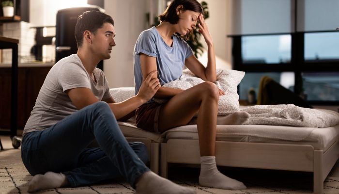Young displeased woman ignoring her boyfriend who is trying to apologize after a quarrel in the bedroom.